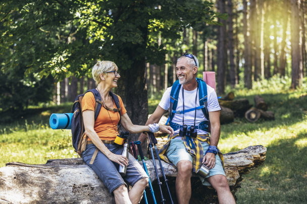 Mature couple sitting and resting in the forest after hiking. - Foto, afbeelding