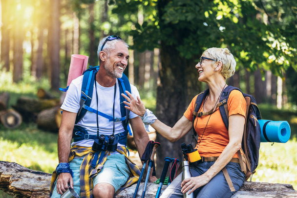 Mature couple sitting and resting in the forest after hiking. - Photo, Image