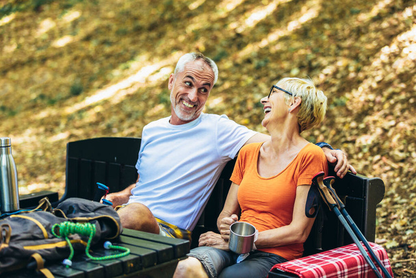 Mature couple sitting and drink coffee while resting in the forest after hiking. - Foto, afbeelding