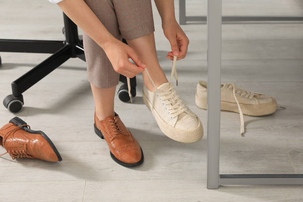Woman taking off uncomfortable shoes and putting on sneakers in office, closeup - Foto, Imagem
