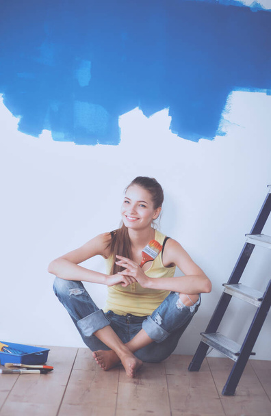 Portrait of female painter sitting on floor near wall after painting. - Foto, afbeelding