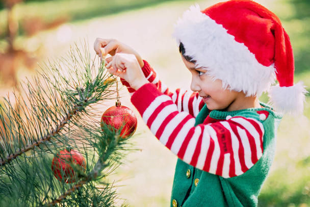 Christmas in july. Child waiting for Christmas in wood in summer. portrait of boy decorating christmas tree. winter holidays and people concept. Merry Christmas and Happy Holidays - Foto, afbeelding