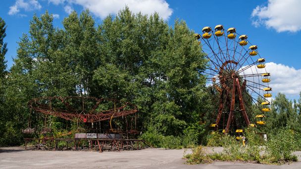 Rusty carousel and ferris wheel in ghost city Pripyat after explosion fourth reactor Chernobyl nuclear power plant. Exclusion radioactive zone on sunny summer day, Ukraine. Radiation, catastrophe - Foto, Bild