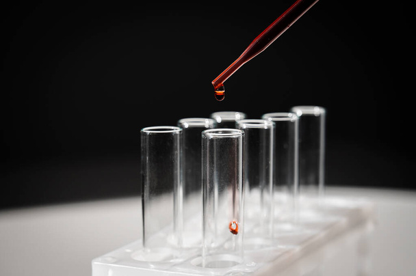Close-up of a laboratory assistant dripping blood from a pipette into a test tube - Foto, Bild