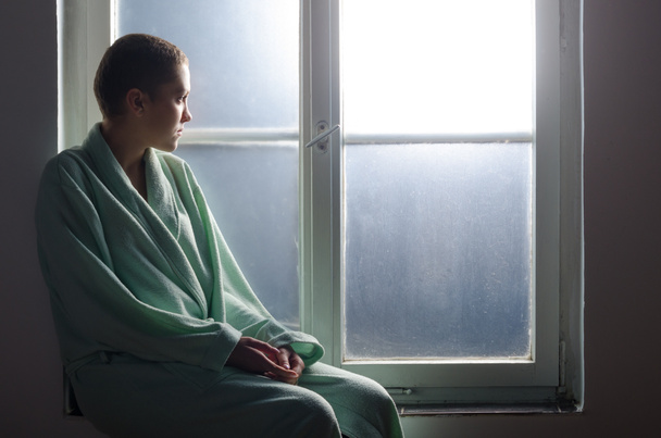 Молодой больной раком сидит перед больничным окном
 - Фото, изображение