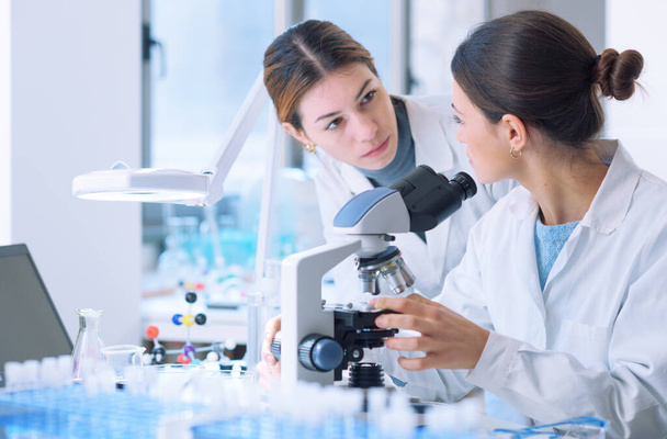 Young female researchers working together in a medical lab, they are examining samples with a microscope - Foto, Imagen