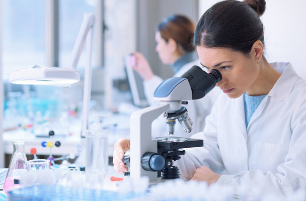 Students doing research in the clinical laboratory, a researcher is using a microscope in the foreground, scientific research concept - Foto, Imagem