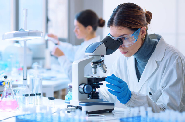 Young scientists conducting research investigations in a medical laboratory, a researcher in the foreground is using a microscope - Foto, immagini