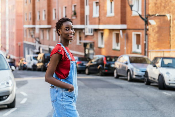Νεαρή μαύρη Αφρικανή μοντέλο που διασχίζει το δρόμο μιας πόλης χαμογελαστή. Υψηλής ποιότητας φωτογραφία - Φωτογραφία, εικόνα