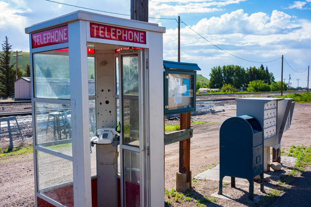 A telephone box that once had a paid telephone, is rewired with a standard telephone that is set in rural scene near railroad tracks along a dirt road on a sunny day.  - Foto, immagini