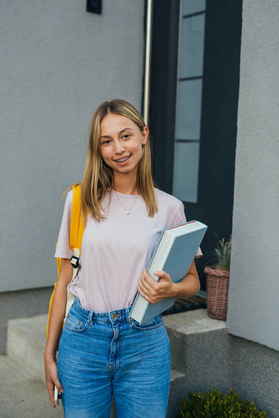 caucasian teenager standing in front of her home with backpack and book - Fotografie, Obrázek