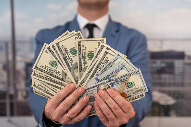 handsome influential man stylishly dressed holding earned money in the form of dollars in front of him. Businessman profit concept - Photo, image