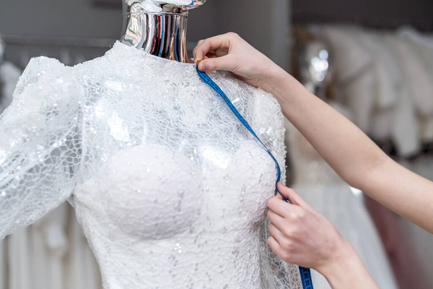 κοντινό πλάνο της γυναίκας σχεδιαστή μοδίστρα χέρι τοποθέτηση νυφικό φόρεμα με ταινία μέτρο σε μπουτίκ - Φωτογραφία, εικόνα