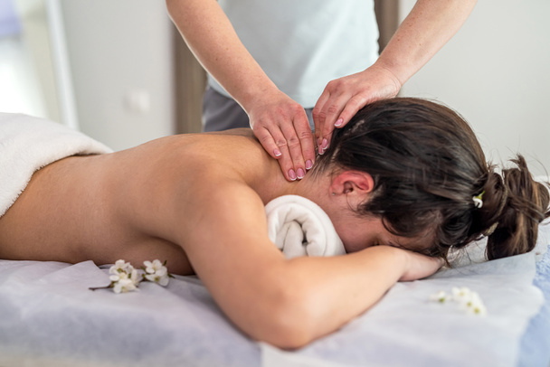 молодая женщина получает ручной расслабляющий массаж на шее, лежащей на столе в спа-салоне. лечебный массаж. - Фото, изображение