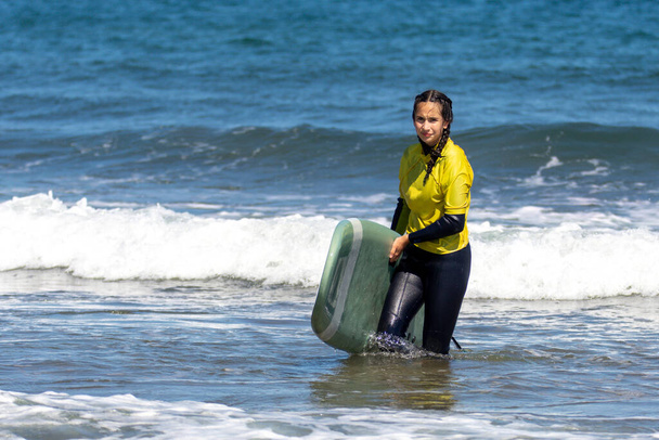 Молодая кавказка выходит из морской воды с доской для серфинга - Фото, изображение