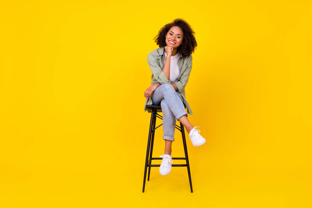 Full body photo of cute young girl wavy hair sit stool smiling banner dressed stylish khaki clothes isolated on yellow color background. - Фото, изображение