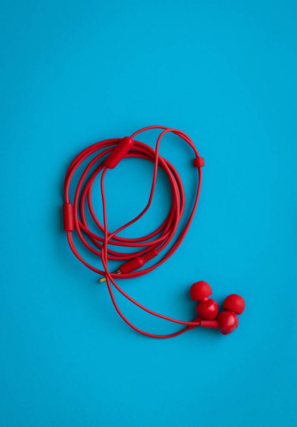 A top view of red earphones with rolled wire on blue background - Foto, immagini