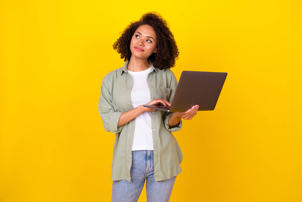 Photo of dreamy millennial brunette lady hold laptop look up wear grey shirt jeans isolated on yellow color background. - Foto, immagini