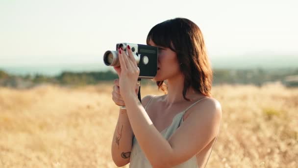 Девушка с короткими волосами делает винтажное видео с 8-миллиметровой камерой в сельской местности.  - Кадры, видео