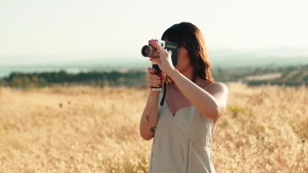 Девушка с короткими волосами делает винтажное видео с 8-миллиметровой камерой в сельской местности.  - Кадры, видео