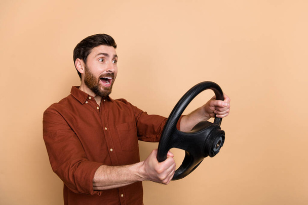 Photo of impressed funny person hold wheel look empty space open mouth isolated on beige color background. - Zdjęcie, obraz