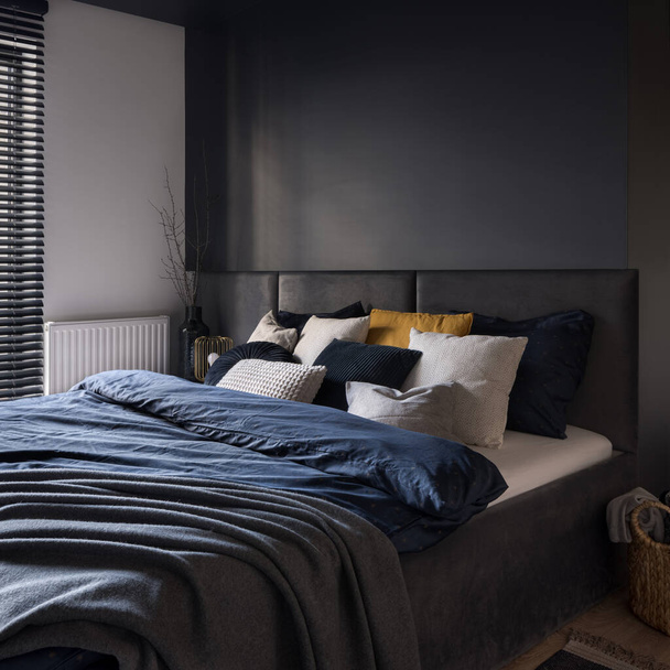 Big and cozy bed in modern and dark bedroom with gray wall and headboard - Foto, immagini