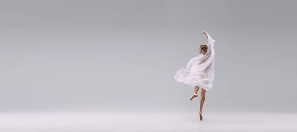 Портрет молодої балерини, вкритий білою прозорою тканиною, ізольовано на сірому студійному фоні. Класичні рухи. Концепція класичного балету, натхнення, краси, танцю, творчості
 - Фото, зображення