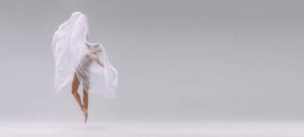 Портрет молодой балерины, покрытый белой прозрачной тканью и танцующий изолированно на сером фоне студии. Грациозный художник. Концепция классического балета, вдохновения, красоты, танца, творчества - Фото, изображение