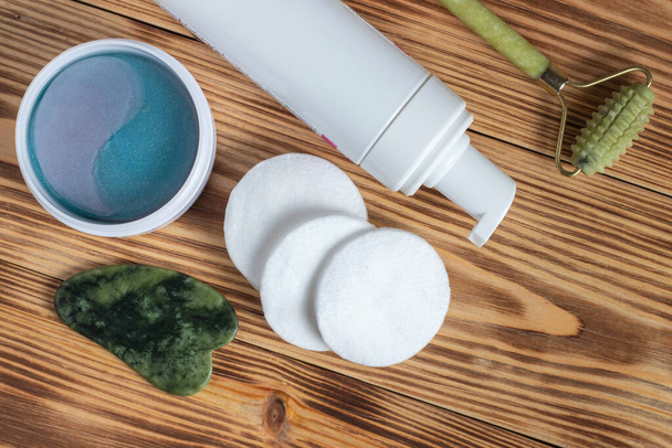 Set of cosmetic tools for self-care. Face rollers, massager gua sha scraper, cosmetic collagen patches on white tray on wooden background. Skin care lifestyle. - 写真・画像