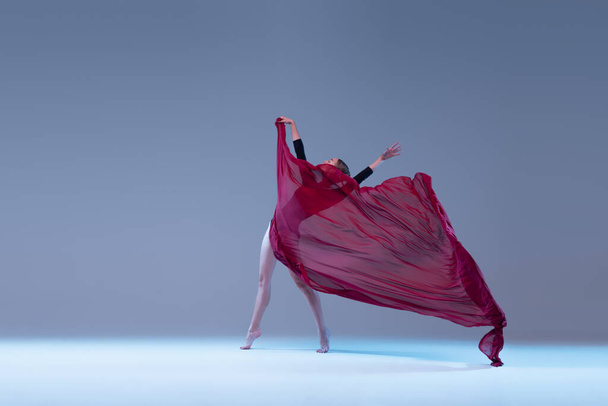 Portrait of young ballerina dancing with fabric isolated over blue grey studio background. Fully covered in deep red cloth. Concept of classic ballet, inspiration, beauty, dance, creativity - Φωτογραφία, εικόνα