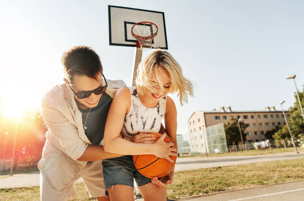 summer holidays, sport and people concept - happy young couple with ball playing on basketball playground - Φωτογραφία, εικόνα