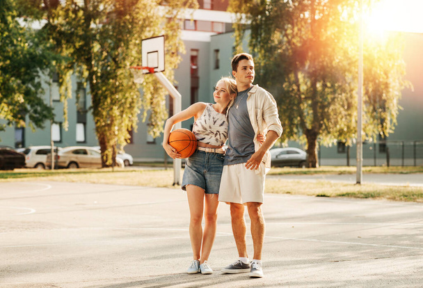 sport, love and people concept - happy young couple with ball hugging on basketball playground - Φωτογραφία, εικόνα