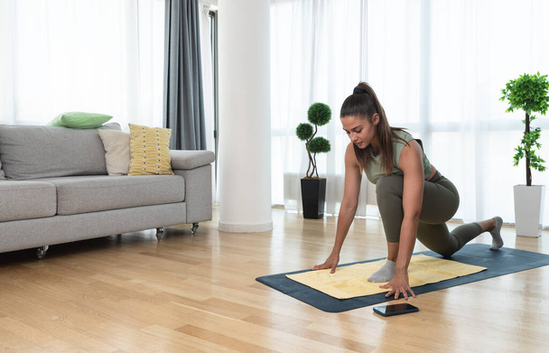 Happy attractive young business woman in active sport wear sitting on stretching muscles at her apartment after or before the work, training yoga class. Home workout as stress and pain relief. - Photo, image