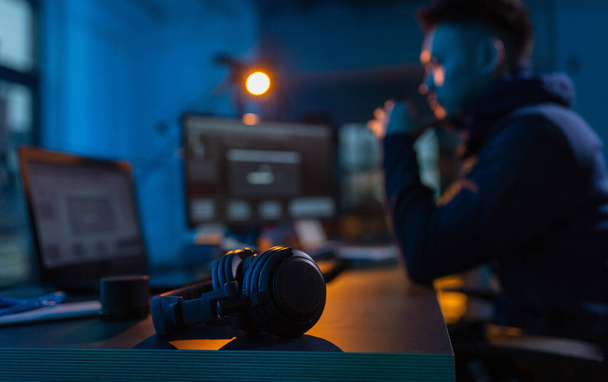 cybercrime, hacking and technology concept - close up of male hacker in dark room with headphones using computer virus program for cyber attack - Фото, изображение