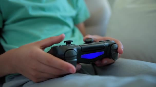 Chłopiec siedzi na kanapie w salonie i gra w gry wideo na konsoli z joyctick gamepad w ręku, rozrywki online i rekreacji - Materiał filmowy, wideo