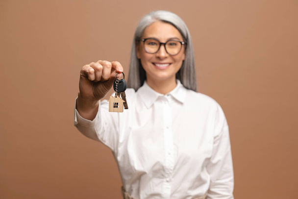 Senior happy woman hold keys of apartments and rejoicing isolated on beige background. People lifestyle concept - Photo, image