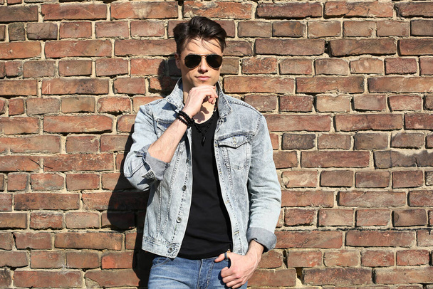 Стильный парень, стоящий на улице в джинсовой куртке на фоне мужской внешности - Фото, изображение
