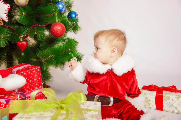 Baby in Santa costume at the Christmas tree - 写真・画像