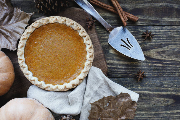 A whole fresh baked pumpkin pie over wood background with ripe pumpkins, cinnamon and star of anise. Top view or flatlay. - Foto, immagini