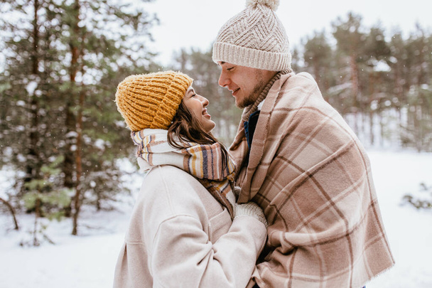 people, love and leisure concept - happy smiling couple looking at each other in winter forest - 写真・画像