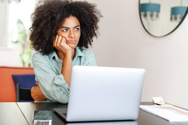 Bored tired african-american woman using laptop for remote work sitting in the living room, female student or freelancer feeling weary or lacks interest in current activity - Foto, imagen