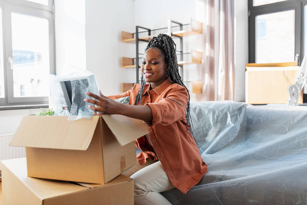 moving, people and real estate concept - happy smiling woman packing boxes sitting on sofa at home - Foto, imagen