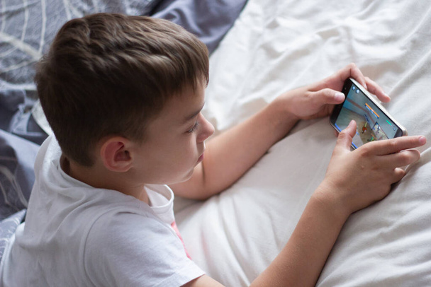 child lying in bed playing on a mobile phone - Foto, Imagem