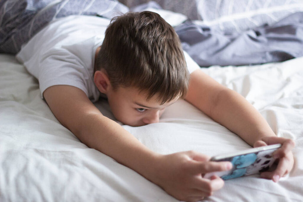 child lying in bed playing on a mobile phone - Foto, immagini