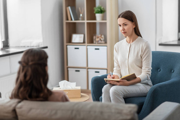 psychology, mental health and people concept - psychologist with notebook and woman patient at psychotherapy session - Foto, Imagem