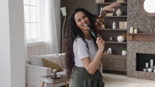 Active funny young woman looking at camera excitedly singing song holding tv remote as microphone having fun at home on weekends amuses dancing vigorously energetic moving to favorite incendiary music - Footage, Video