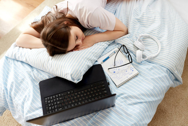 school, education and laziness concept - tired teenage student girl with laptop computer and notebooks sleeping on bed at home - Foto, Imagem