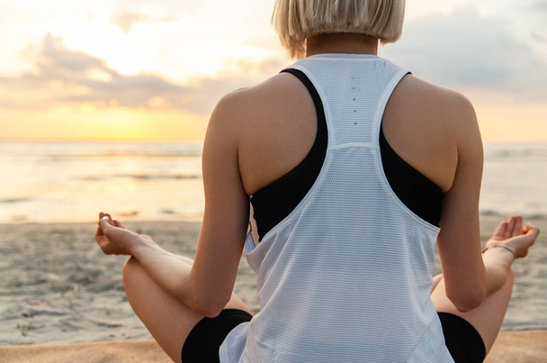 yoga, mindfulness and meditation concept - close up of woman meditating in lotus pose on beach over sunset - Φωτογραφία, εικόνα