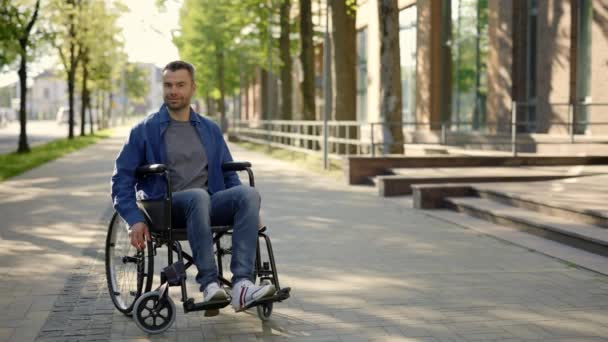 Portrait of the happy man on a wheelchair wearing casual clothes. A disabled smiled man riding in the middle of the day. People and disabled people concept - Séquence, vidéo