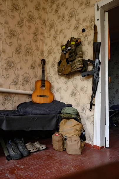 ギターの横にある兵士の戦闘軍事攻撃ライフルAK 74と軍事弾薬、ウクライナの戦争、折り畳まれた軍事靴. - 写真・画像